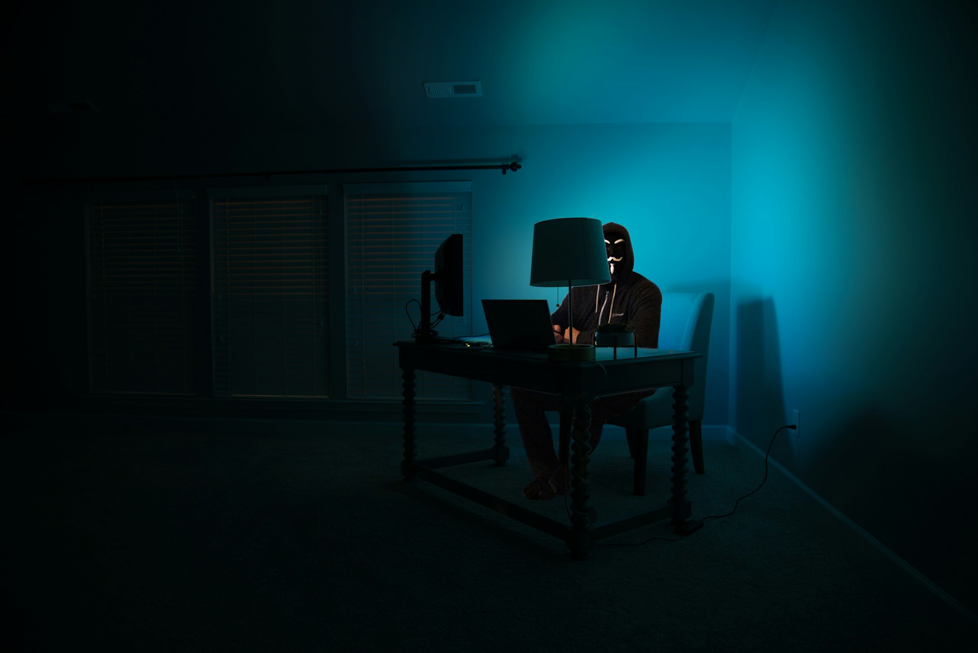 A man at a computer disguised as an anonymous hacker wearing a Guy Fawkes mask. Our cyber security jargon buster article will help you understand some common terms that may be used when he's around!